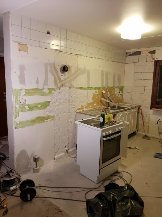 Kök under renovering med borttaget kakel, spacklade väggar och osammanhängande inredning.