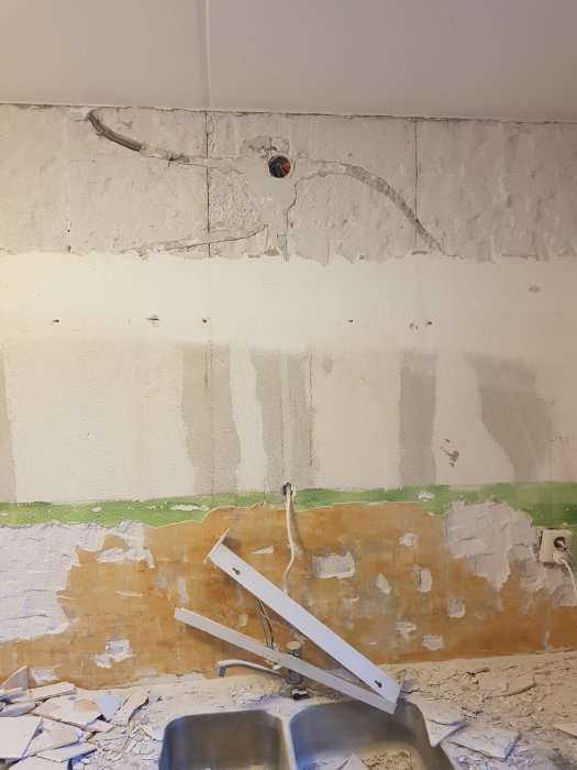 Renoveringsarbete i kök med borttaget kakel och väggar delvis spacklade.