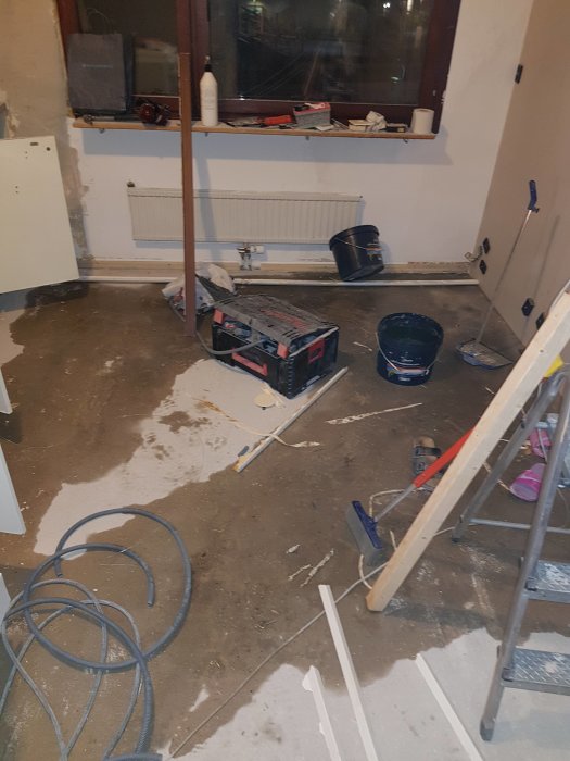 Renoveringsprocess i kök med verktyg, gipsplattor och rör på golvet och spacklade väggar.