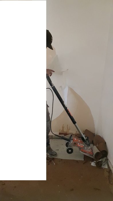 Person använder en betongslip för att ta bort limmad matta från betonggolv.