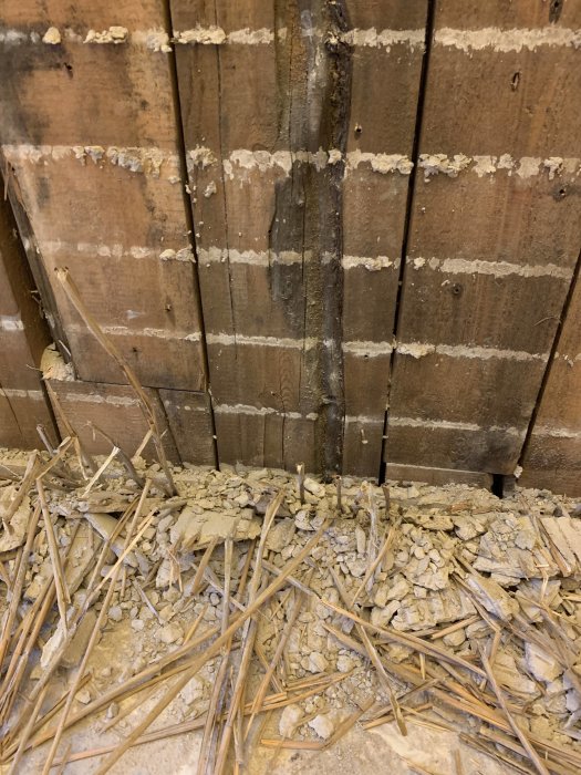 Puuseinä, jossa on vanhaa eristettä ja risuja, joissa on savitiivistettä; kuoriutunut rakenne näkyvissä.