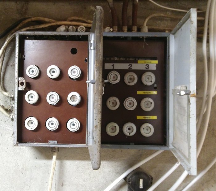Två öppna gamla säkringsskåp med flera säkringsplatser, anslutna kablar och etiketterade områden.