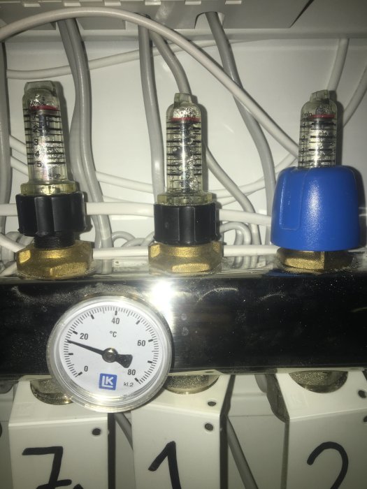 Manometern och vreden på ett värmesystem med rör och kablar i bakgrunden.