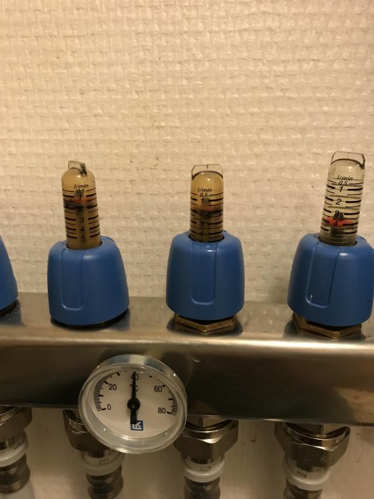 Fem ställdon på en fördelare för värmesystem, fyra mörkare och en genomskinlig som visar flöde.