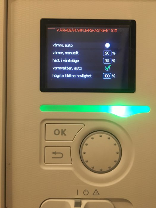 Digital termostat display som visar värmebärarepumpshastigheter och inställningar med belyst grönt ljus ovanpå.