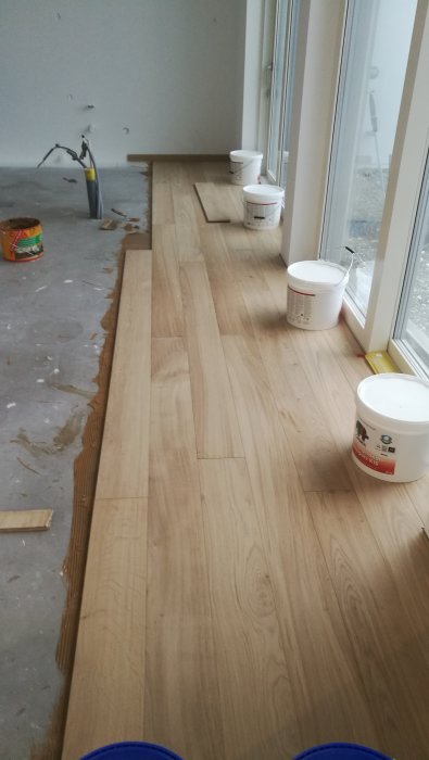 Delvis lagt trägolv i ett rum med verktyg och byggmaterial synliga.