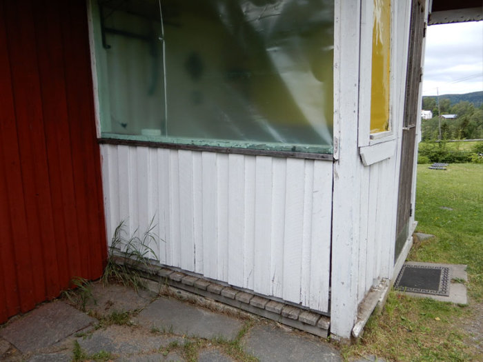 Del av ett hus med vit panel klädd för renovering nära en gammal entré med röda och gula väggar.