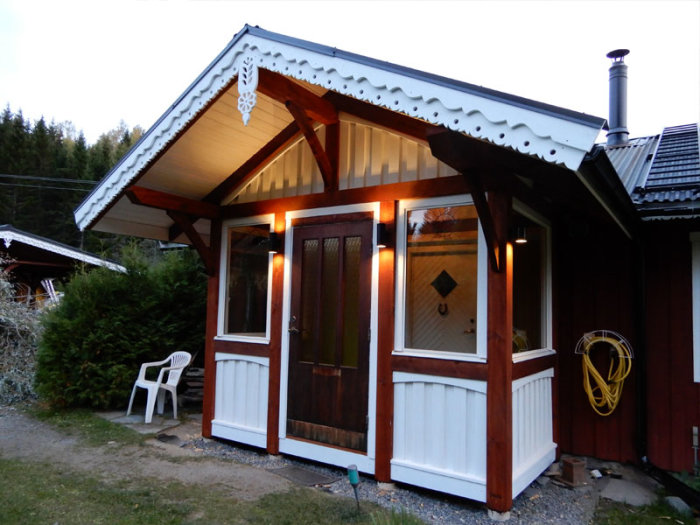 Renoverad entré till hus med ny takplåt, vita väggar och träpaneler, belyst i skymningen.
