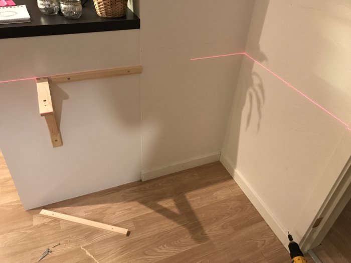 Nyinstallerat vägghängt skrivbord i trä under montering, med laserlinje för räta vinklar.