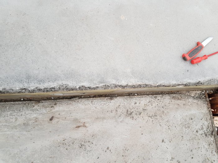 Betongtrappsteg med ojämnt gjutet kant och lossnade betongbitar, två röda mejslar ligger på golvet.