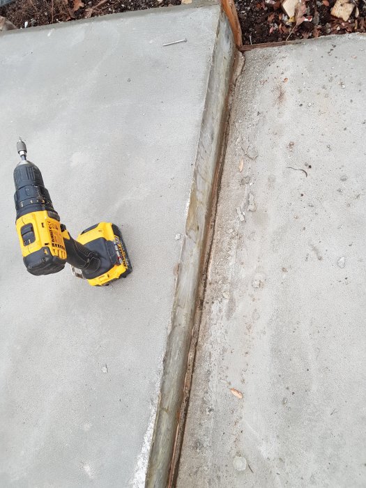 Betongtrappsteg intill en trädgårdskant med en gulsvart skruvdragare på marken.