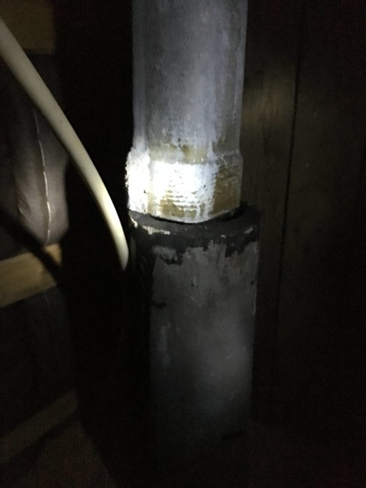 Oisolerat ventilationsrör med synlig skarv på en vind, upplyst i dunkelt ljus, med tecken på kondens.