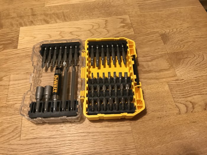 En öppen Dewalt bitssats med ordnade borr och bits på ett trägolv.