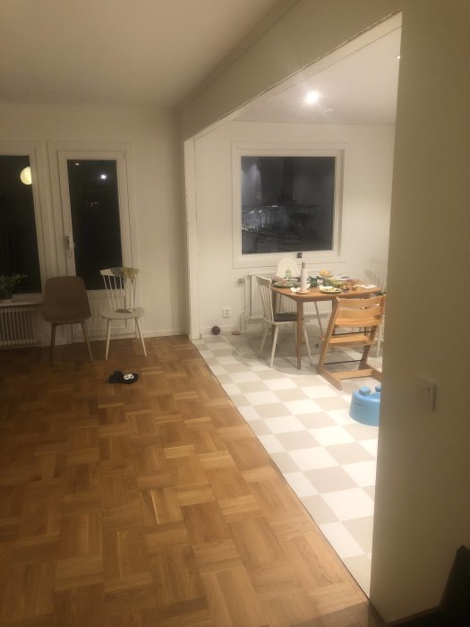 Öppning mellan kök med ekparkett och vardagsrum med linoleumplattor i samma nivå.