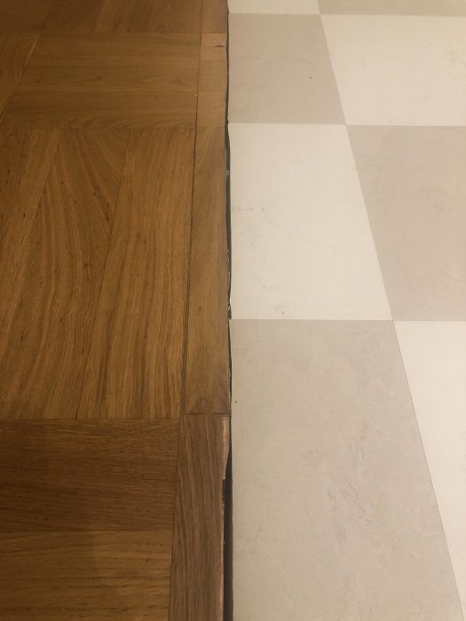 Övergång mellan ett mörkt trägolv och ljus klinker utan list, möjlig plats för mässingslist.