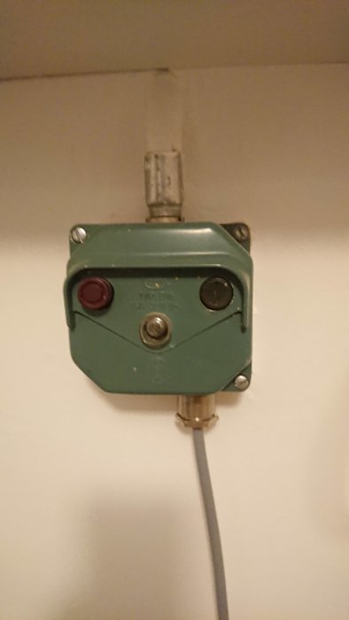 Industriell strömbrytare på vägg med röd och svart knapp, ledning ansluten.