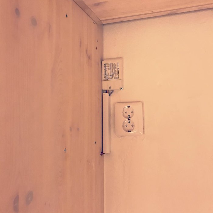 Elektrisk installation med synliga kablar och eluttaget på väggen bakom en träpanel, utförd av en elektriker.