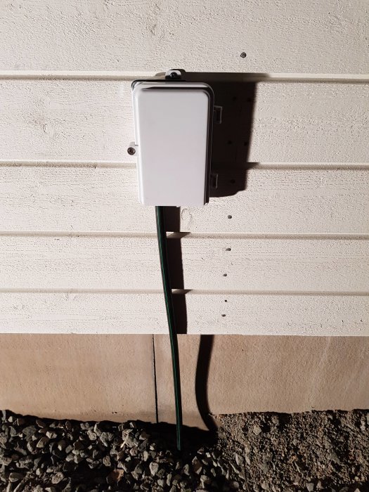 Omvandlarrouter installerad på husvägg med en grön fiberkabel som löper neråt längs väggen.