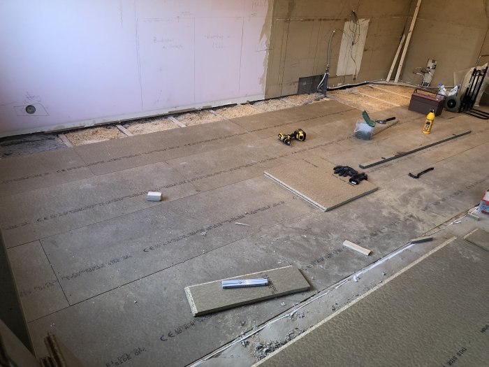 Uppbrutet golv under konstruktion med nya spångolv delar och verktyg utspridda på ytan.