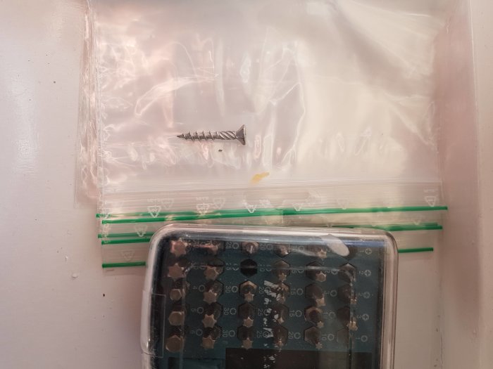 En skruv i en genomskinlig plastpåse ovanpå en digital våg mot en vit bakgrund.