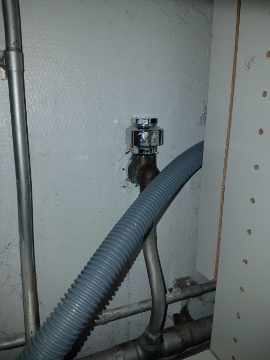 Vattenutkastare med ansluten vakuumklocka och slang, monterad på en vit vägg, visar tecken på läckage.