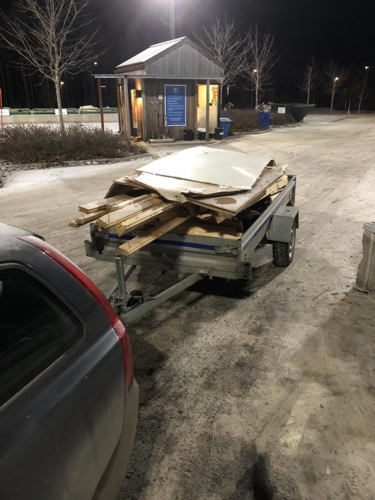 Släpvagn fylld med byggavfall parkerad på en återvinningscentral om natten.