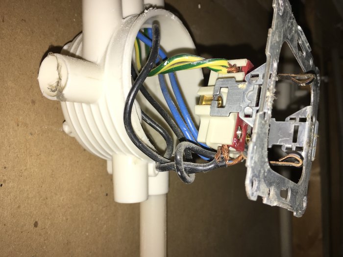 Öppen kopplingsdosa med eluttag och synliga sladdar som hänger från taket under pågående renovering.