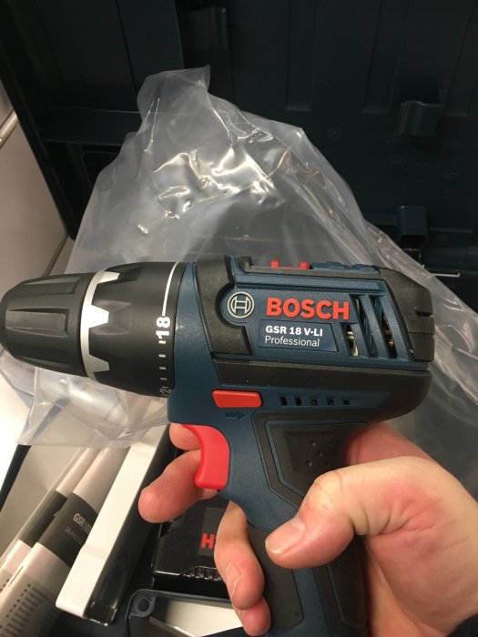 Hand håller en Bosch GSR 18 V-LI Professional borrskruvdragare med förpackning i bakgrunden.