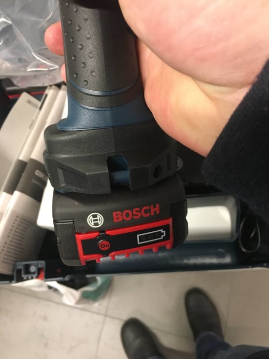 Hand som håller en BOSCH borrskruvdragare, synlig från batteridelen, med fokus på märkeslogotypen.