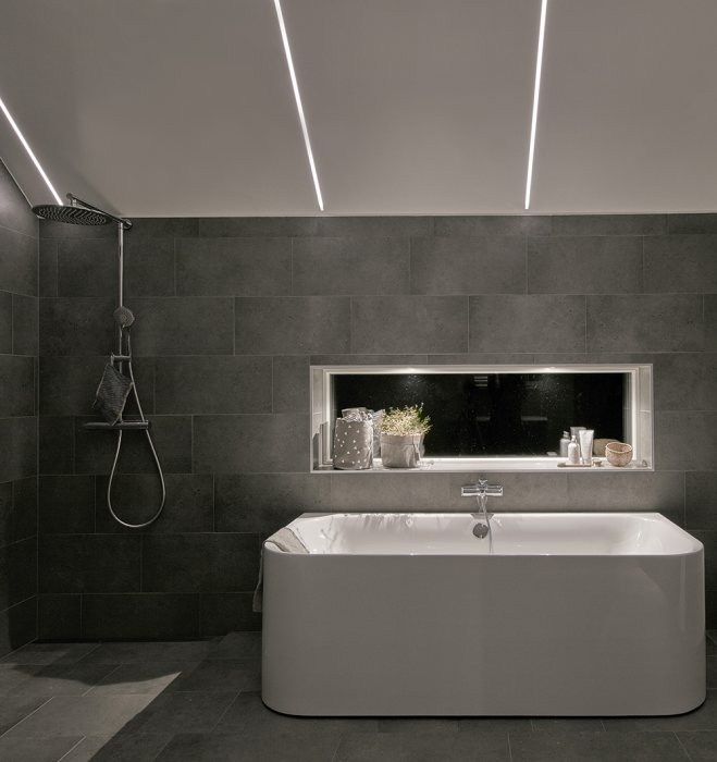 Modernt badrum med infällda aluminiumprofiler i taket som skapar en linjär ljusdesign.