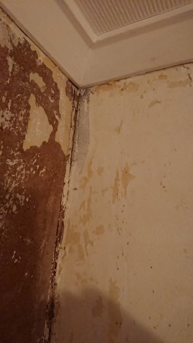 Vitt material på betongvägg i hörn bredvid vägg med brun träskiva, ojämna ytor och avflagningar.
