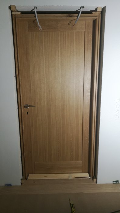 Nyinstallerad träfärgad dörr i karm med synliga elledningar och verktyg på golvet.