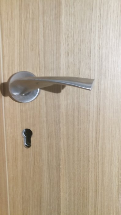 Nyinstallerad dörrhandtag och låscylinder i en ljus träfärgad dörr.