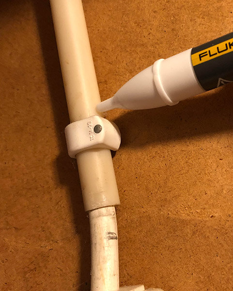 Spänningsprovare av märket Fluke nära en vitledning och koppling, använd för att snabbt kontrollera elektrisk spänning.