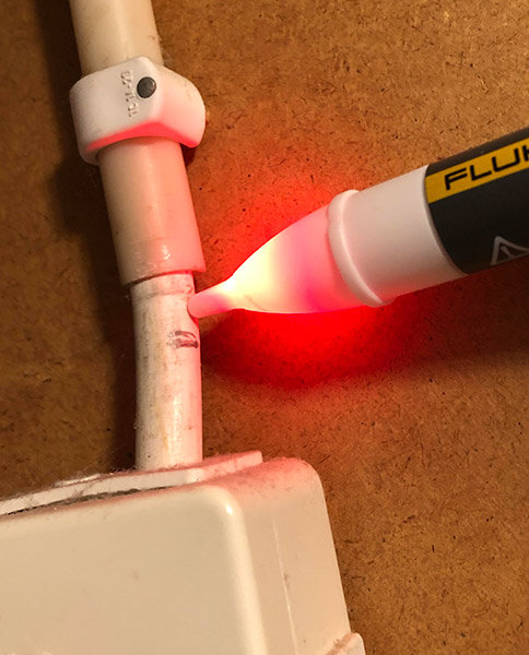 Fluke spänningsprovare med lysande spets nära en elinstallation som indikerar närvaro av spänning.