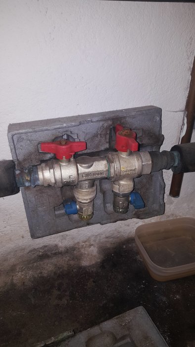 VVS-installation med en öppen och en stängd röd ventil samt en skål under på en betongyta.