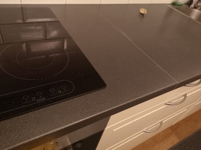 Svullnad på en del av köksbänkskiva nära spishäll, möjlig fuktskadeindikation.