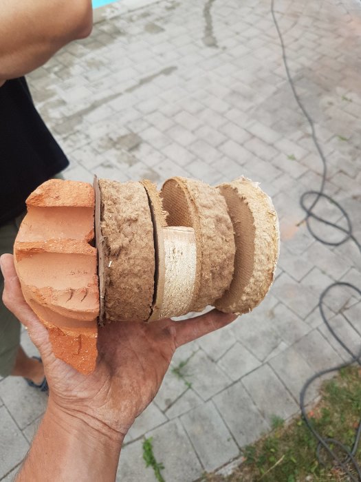 Genomskärning av en yttervägg med lager av tegel, isolering och ångspärr, hålls upp av en hand.