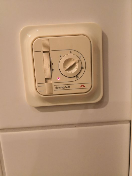 Termostat av modellen Devireg 520 monterad på vägg med justeringsratt inställd mellan 4 och 6.
