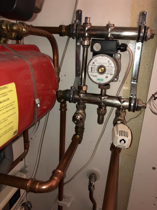 Värmesystem med cirkulationspump och kopparledningar, röd expansionskärl och termostatinställning.