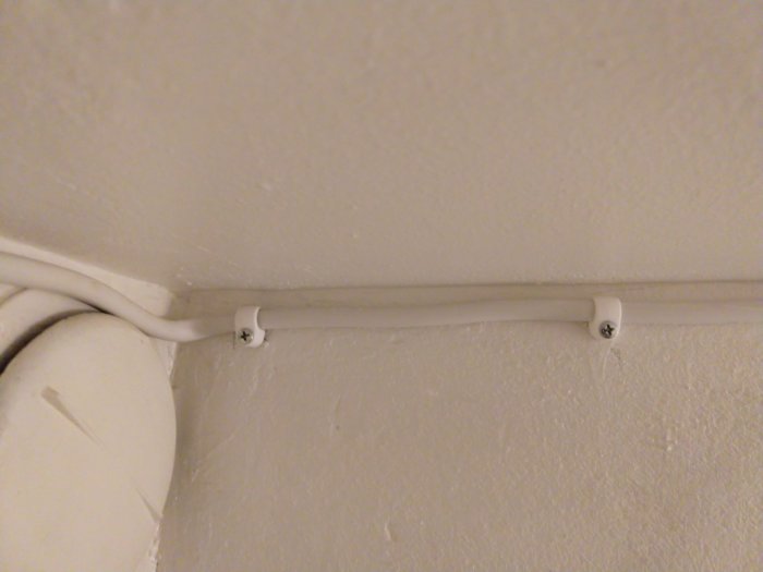 Elkabel dragen slarvigt längs ett hörn mellan tak och vägg med synliga klamrar och ojämn förläggning.