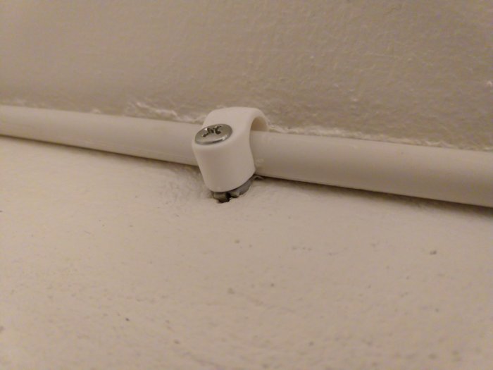 Dåligt installerad elektrisk kabel med klumpig klammer och löst sittande i hörnet där tak möter vägg.