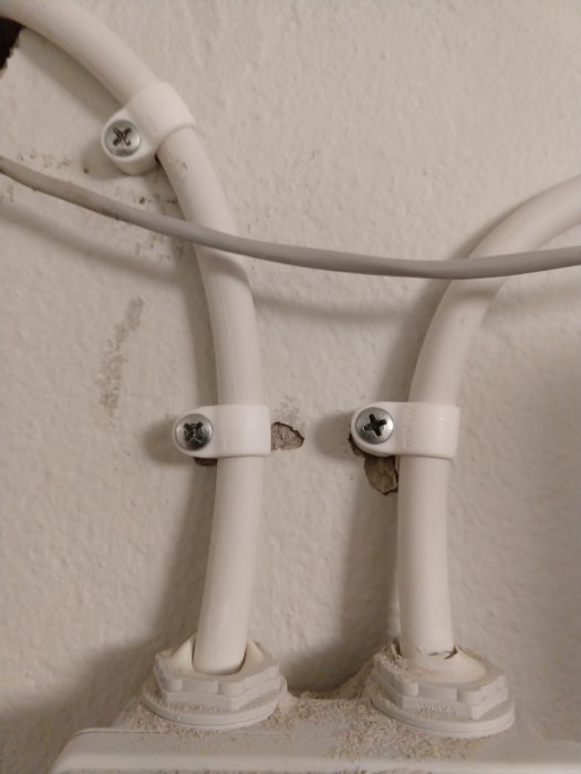 Oprofessionellt utförd elektrisk kabeldragning i vinkel av vägg och tak med klumpiga klamrar.