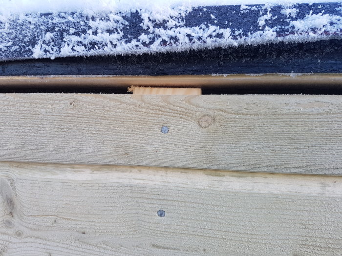 Nyinstallerad träpanel med synliga skruvar under ett snötäckt takutsprång.