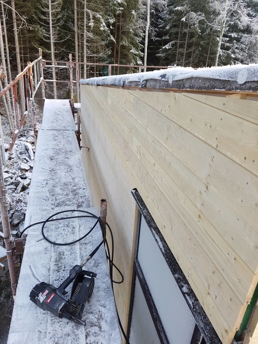 Nyinstallerad träpanel på byggnadsställning med snö, verktyg och byggmaterial i förgrunden.