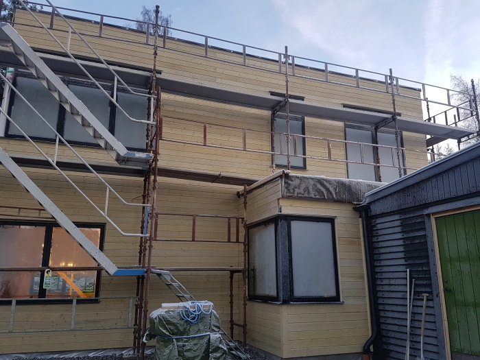 Hus under renovering med nyinstallerad panel och ställningar runt byggnaden.