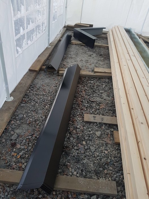 Ny panel och svart plåt på grusgolv i ett byggtält.