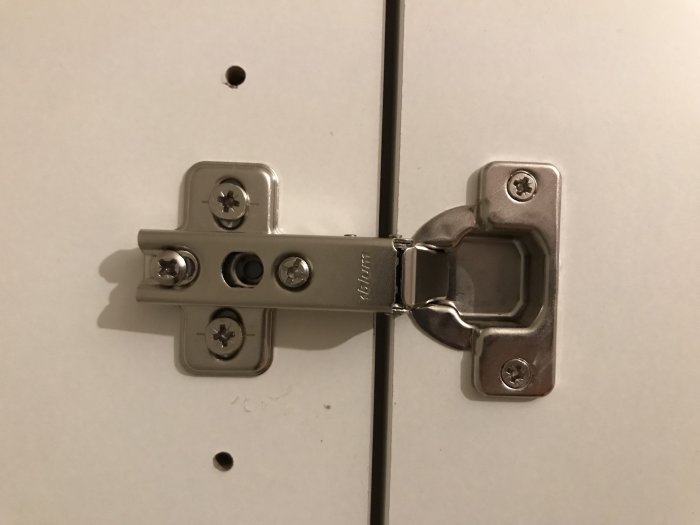 Närbild på en oupphängd garderobsdörr med justerskruvar och ett osäkrat mittskruvhål.