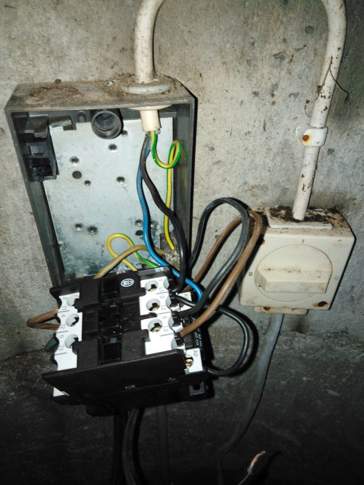 Öppet elektriskt skåp med ny kontaktor, förvirrande kablage, närliggande strömbrytare och rörtillförsel.