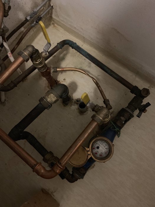 Vatteninstallation med rör, ventiler och en mätare i ett pannrum.